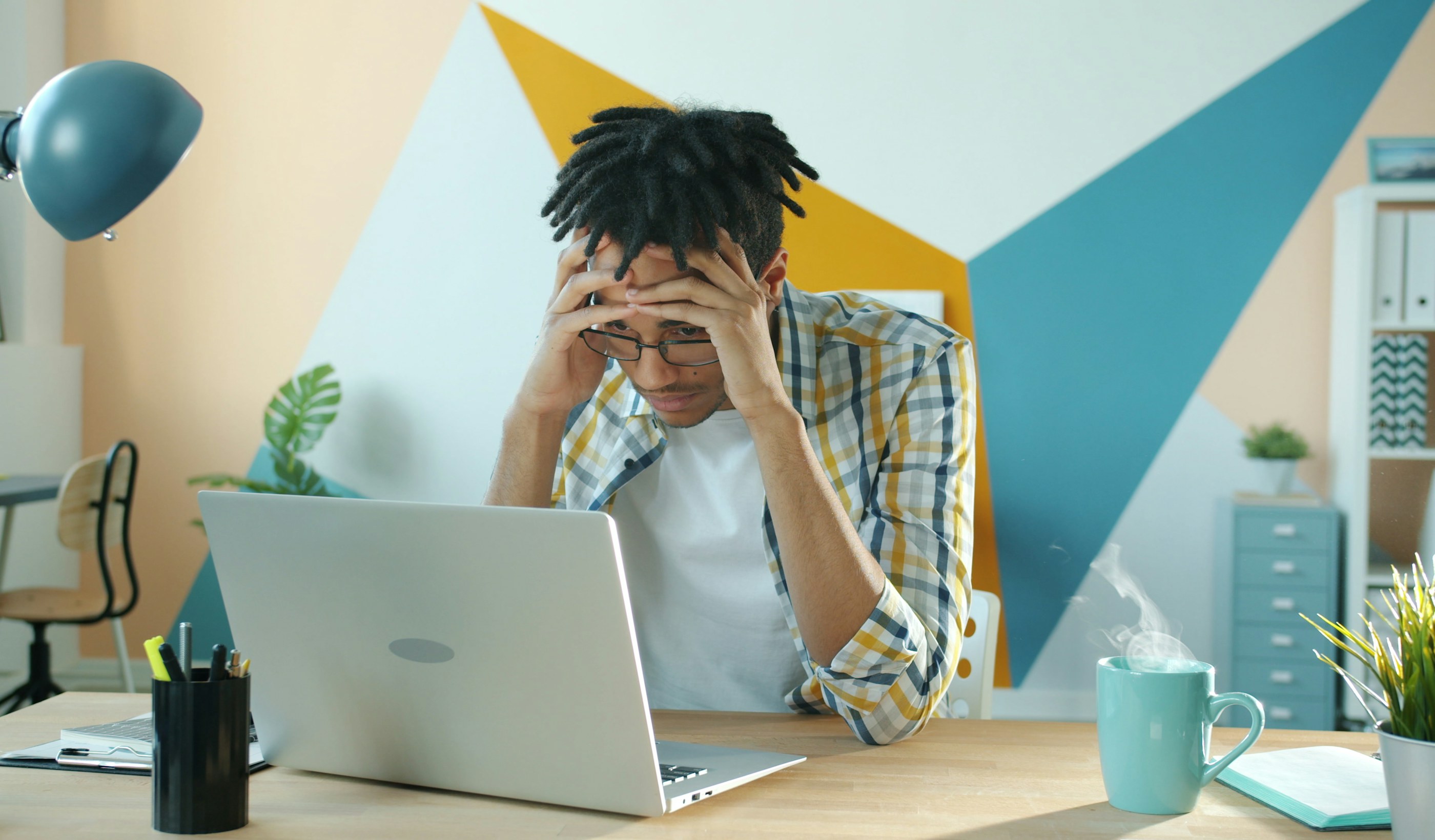 A person holding their head in frustration at a desk with a laptop