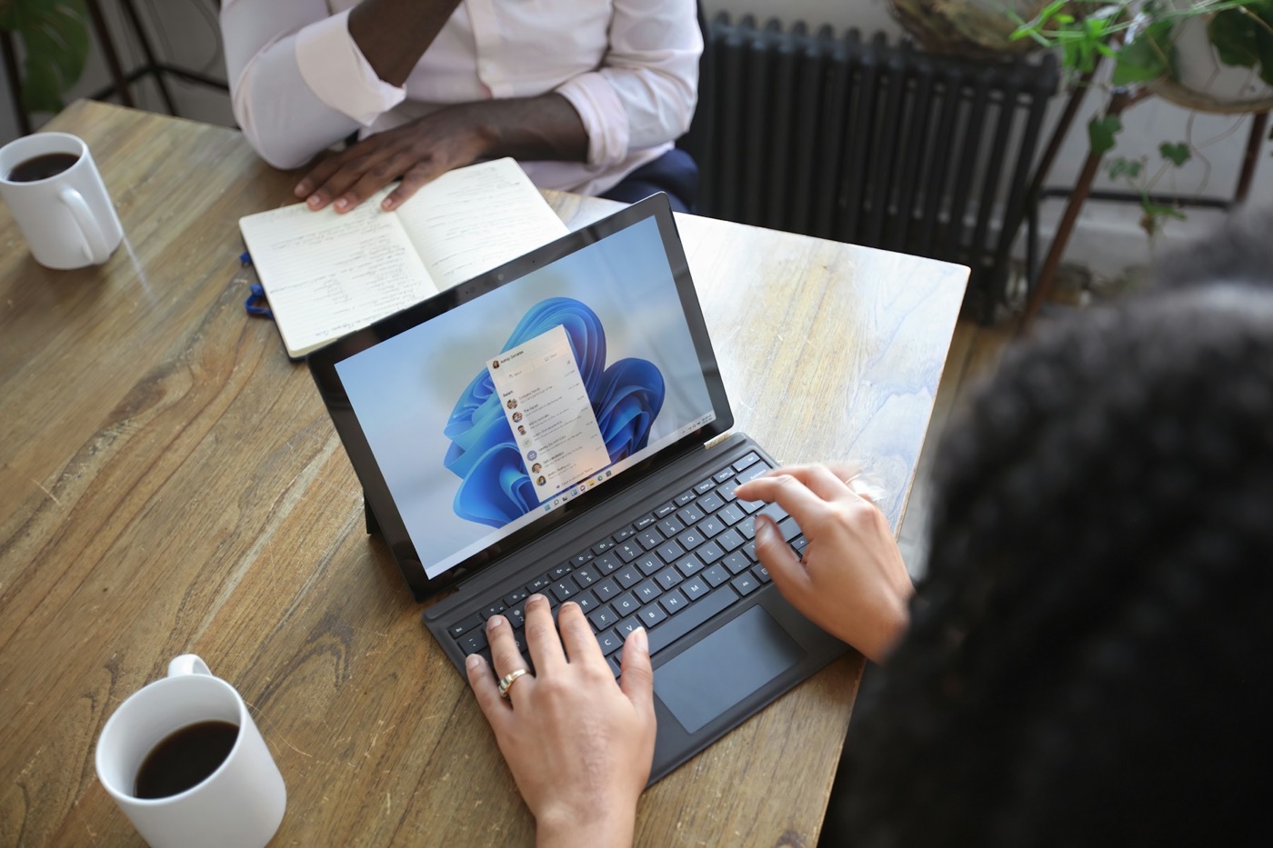 Overhead view of two people at a wooden table with a laptop, an open notebook of handwritten notes and two coffees