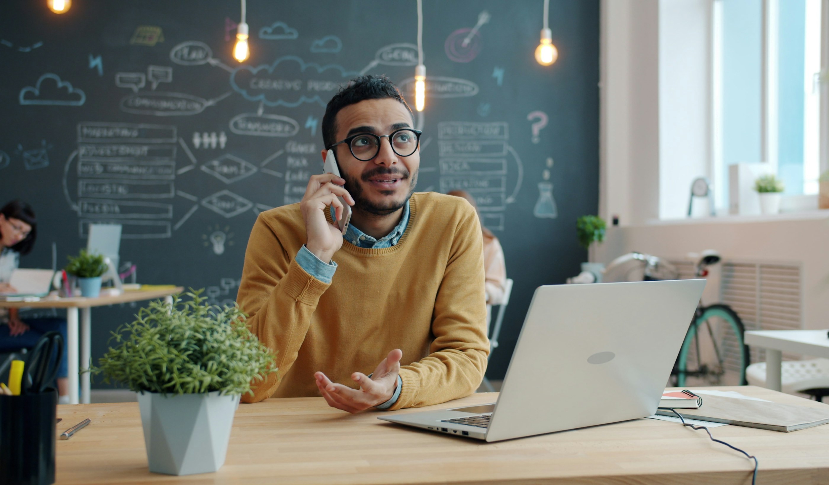 A salesperson at a desk on a phone call beside an open laptop