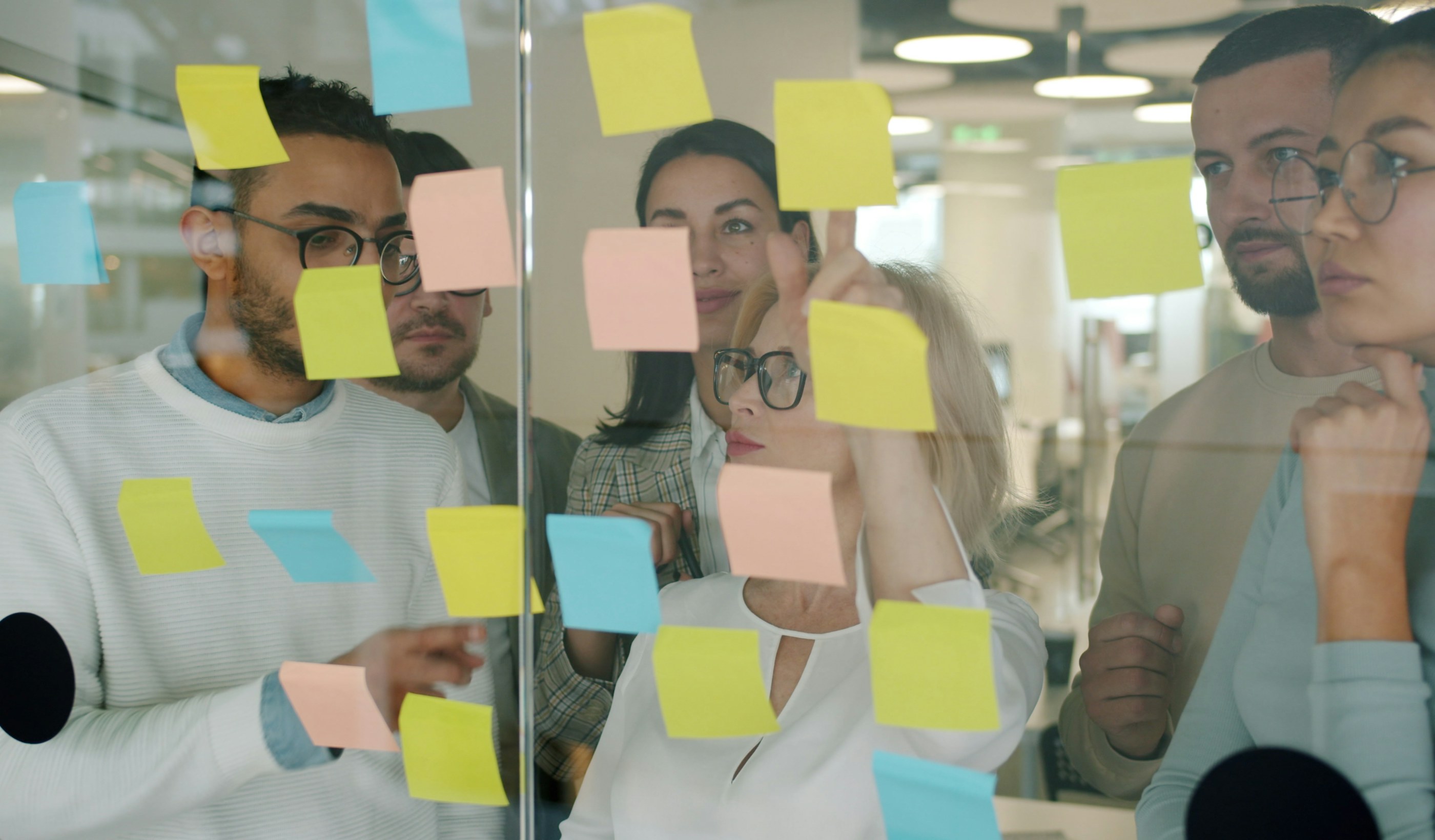 A team standing at a glass wall covered in coloured sticky notes during a working session