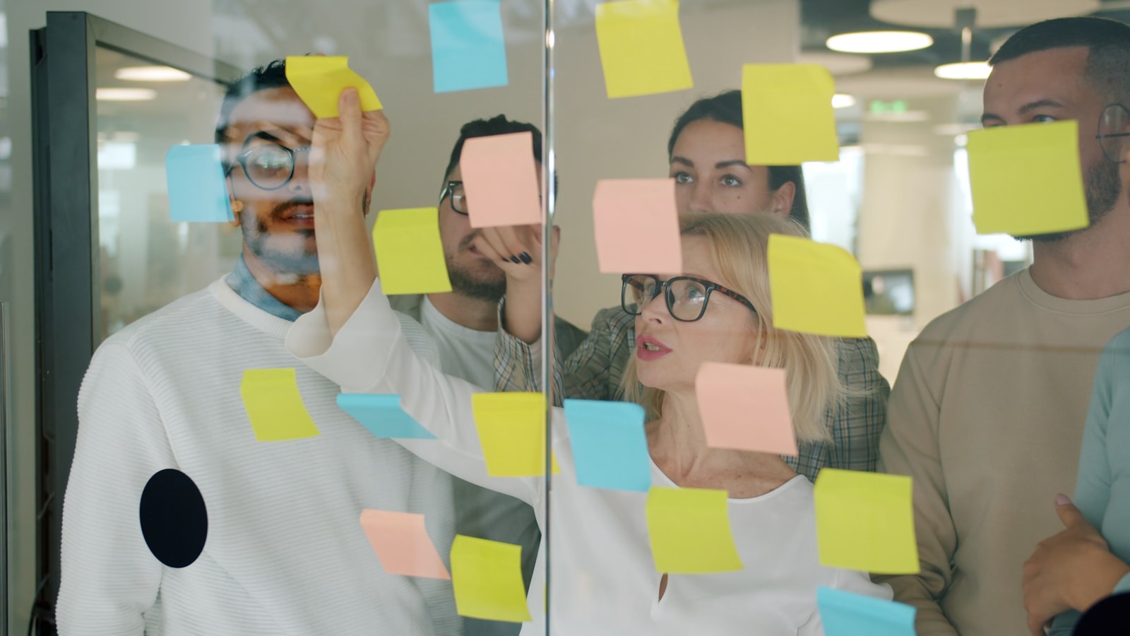 A team brainstorming with colourful sticky notes stuck to a glass wall in an office