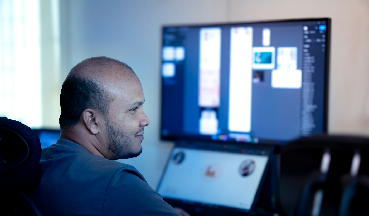 A man reviewing work on a large computer monitor in an office