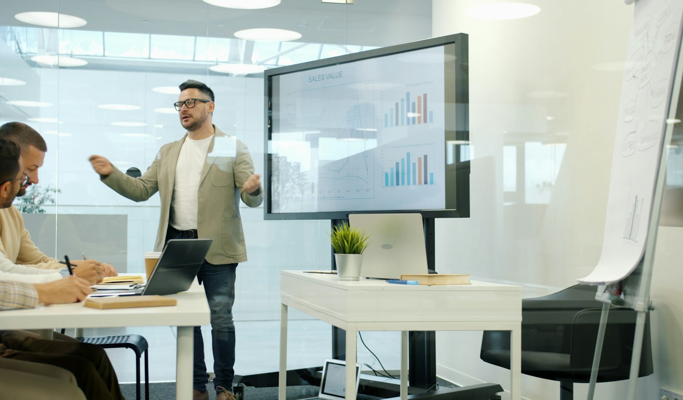A colleague presenting sales charts on a large screen in a meeting room