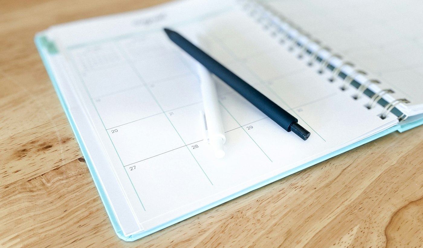 An open paper planner with a pen resting on it on a wooden desk