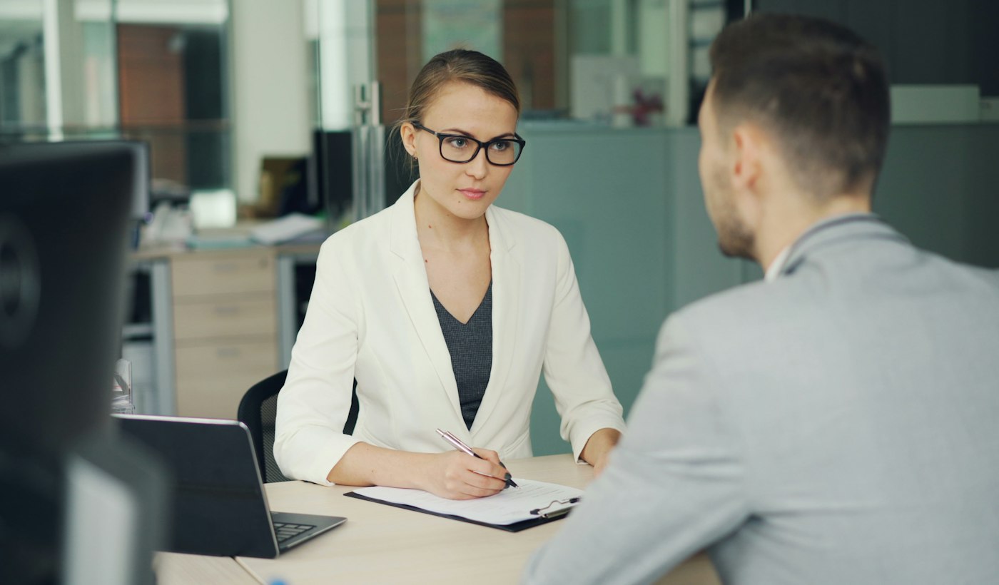 A woman interviewing a colleague across an office desk