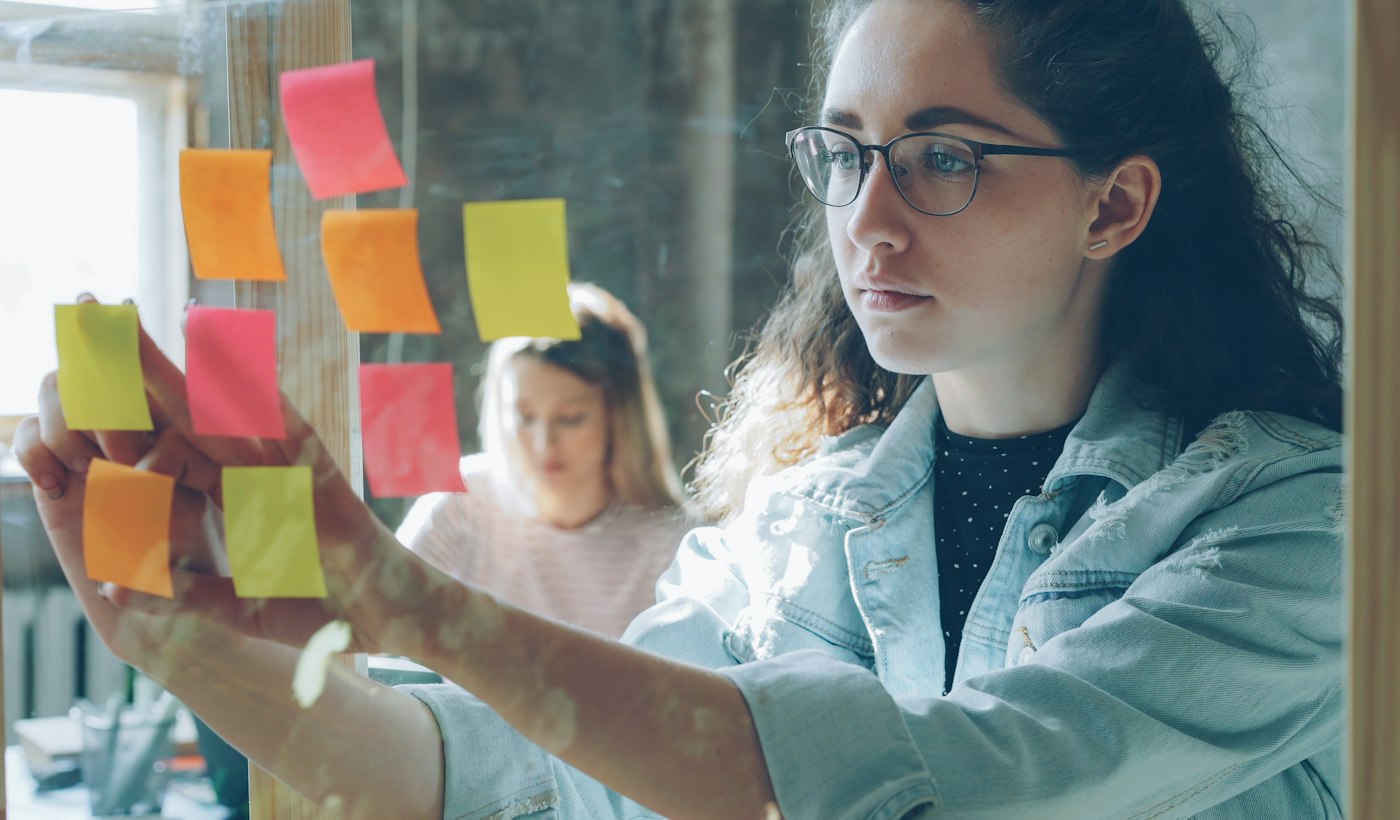 A person arranging coloured sticky notes on a glass wall