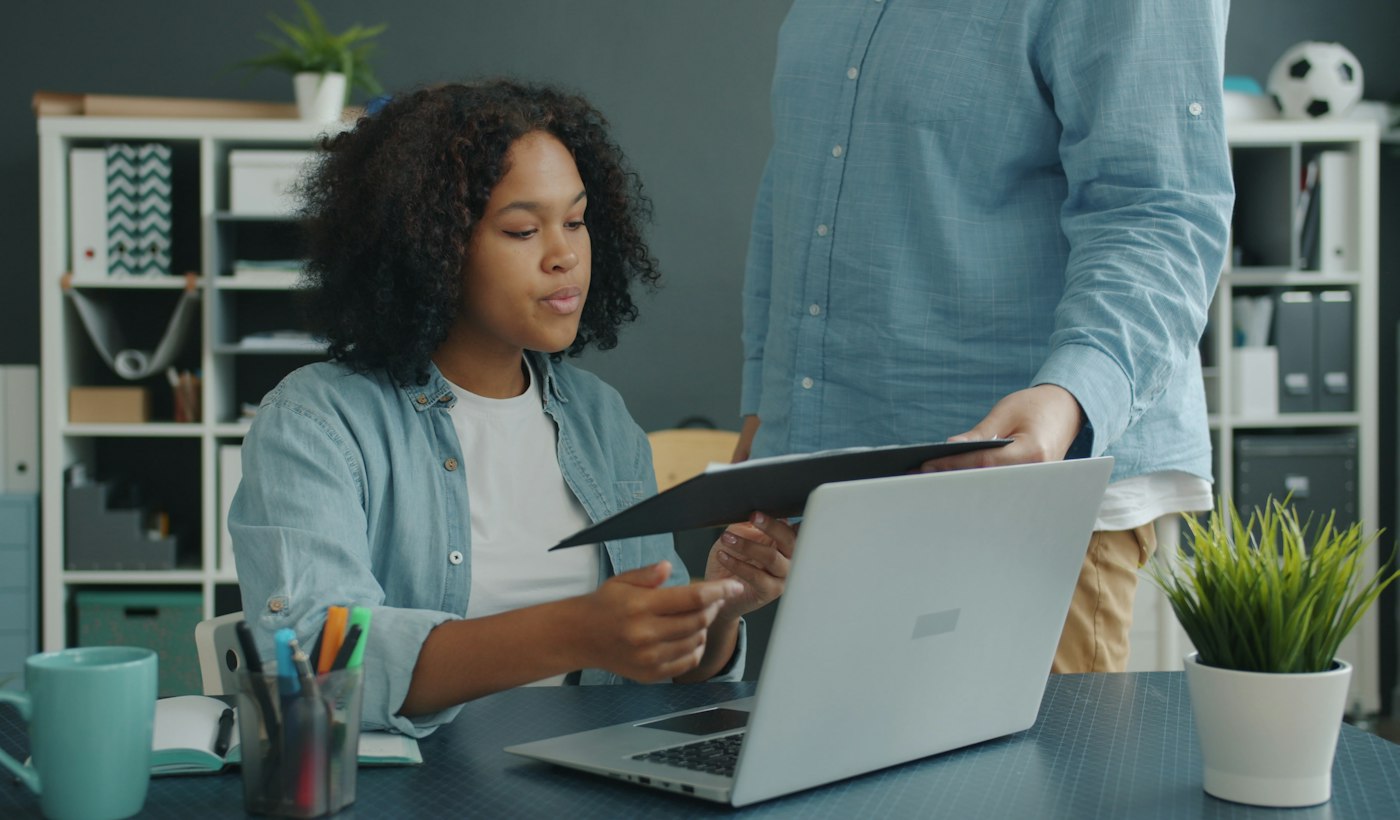 Two colleagues reviewing documents at an office desk with a laptop