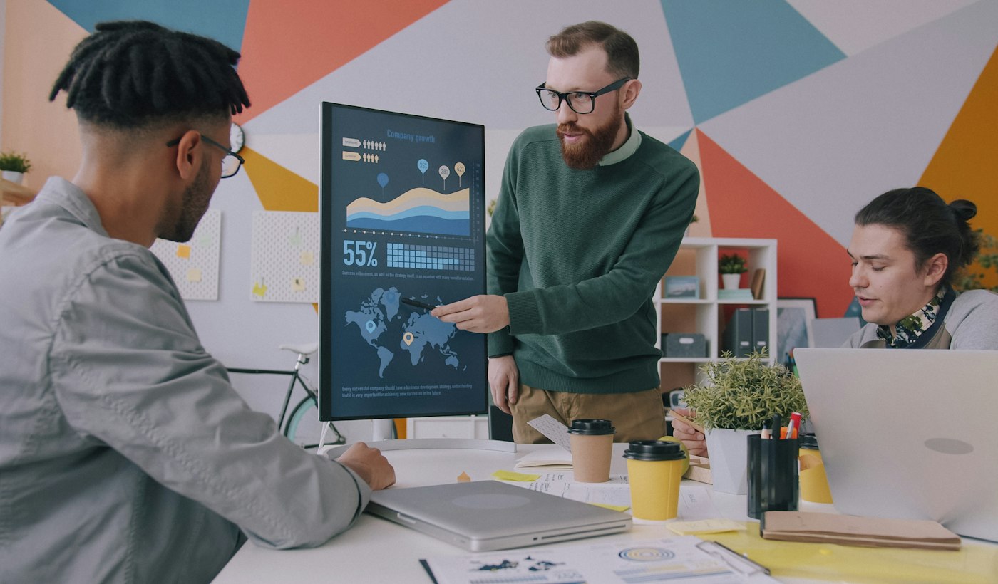 A colleague presenting data on a screen to two people in an office
